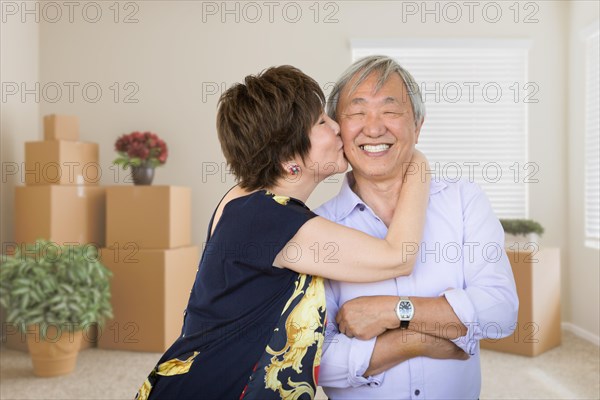 Happy senior chinese couple inside empty room with moving boxes and plants