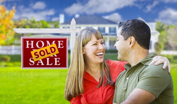 Happy mixed-race couple in front of sold home for sale real estate sign and house