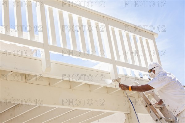 House painter wearing facial protection spray painting A deck of A home