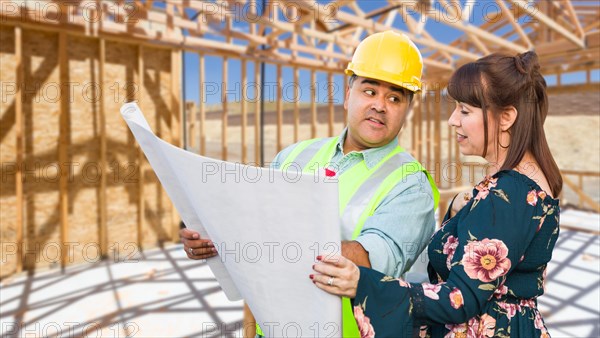 Hispanic male contractor talking with female client over blueprint plans at construction site