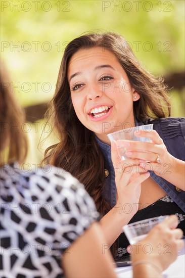 Expressive young adult woman having drinks and talking with her friend outdoors