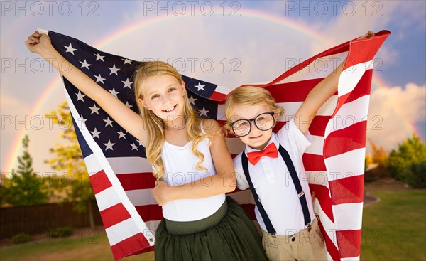 Cute young cuacasian boy and girl holding american flag with rainbow behind