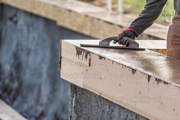 Construction worker using wood trowel on wet cement forming coping around new pool