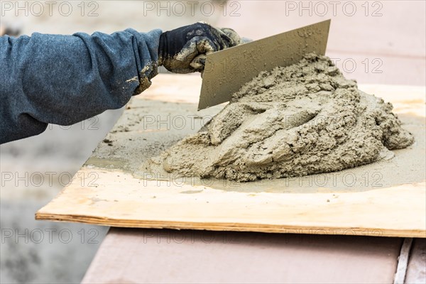 Tile worker mixing wet cement on board at pool construction site