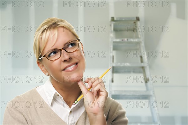 Happy woman holding pencil inside room with new sheetrock drywall and ladder