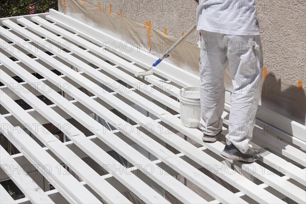 Painter rolling white paint onto the top of A home patio cover