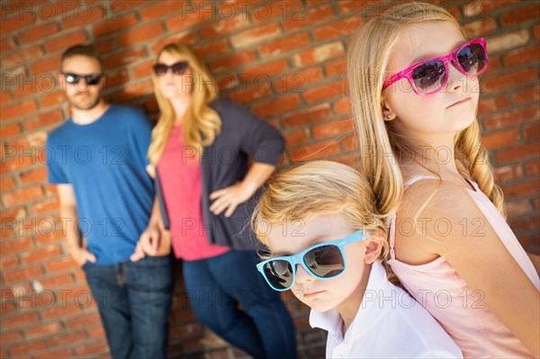 Cute young caucasian brother and sister wearing sunglasses with parents behind