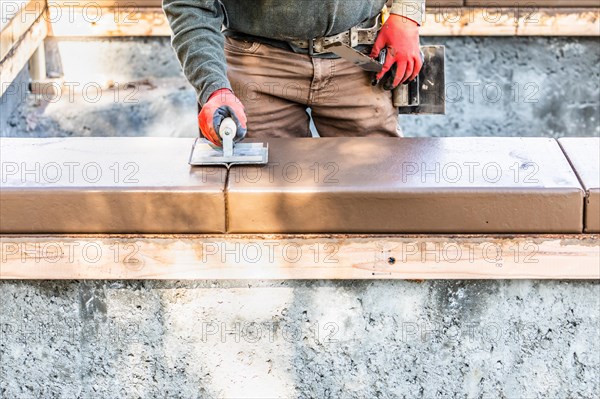 Construction worker using hand groover on wet cement forming coping around new pool