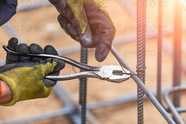 Worker securing steel rebar framing with wire plier cutter tool at construction site