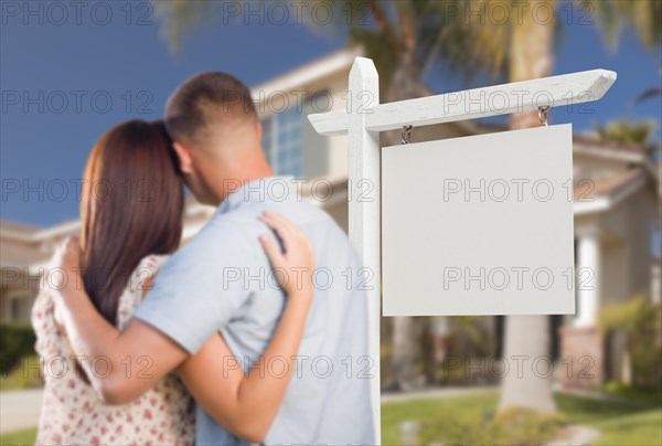 Blank real estate sign and military couple looking at nice new house