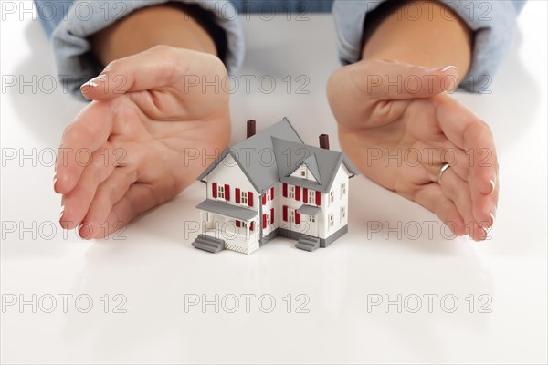 Womans hands around model house on white surface