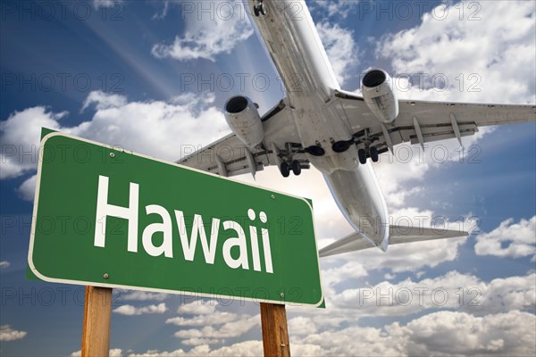 Hawaii green road sign and airplane above with dramatic blue sky and clouds