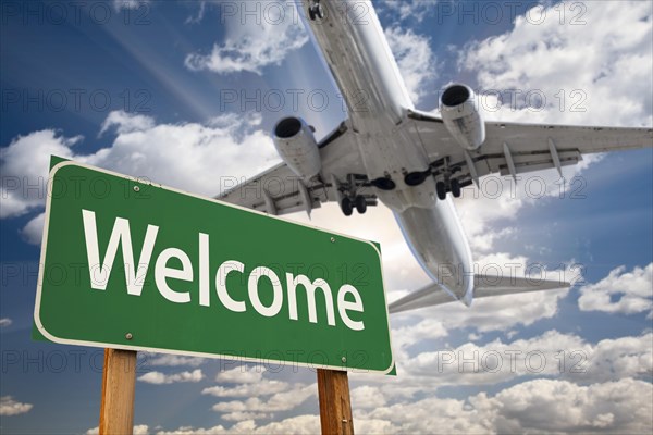 Welcome green road sign and airplane above with dramatic blue sky and clouds