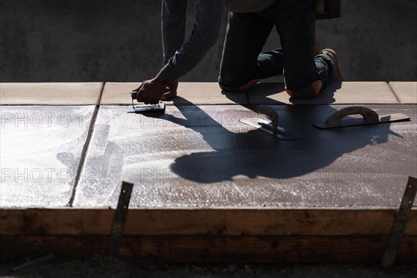 Construction worker smoothing wet cement with hand edger tool