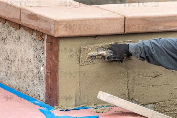 Tile worker applying cement with trowel at pool construction site