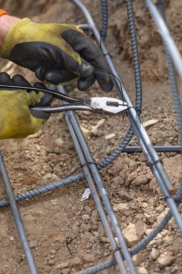 Worker securing steel rebar framing with wire plier cutter tool at construction site