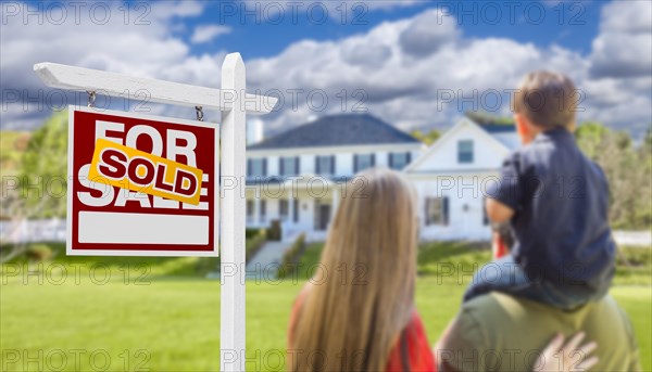 Curious family facing sold for sale real estate sign and beautiful new house