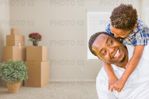 Happy mixed-race african american father and son in room with packed moving boxes