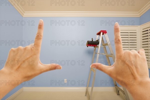 Hands framing blue painted room wall interior with ladder