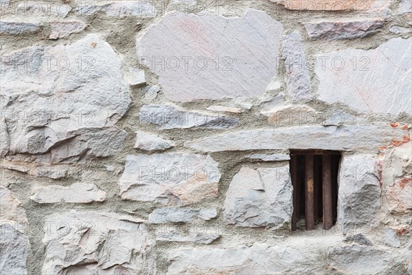 Old stone wall with small iron barred prison cell window