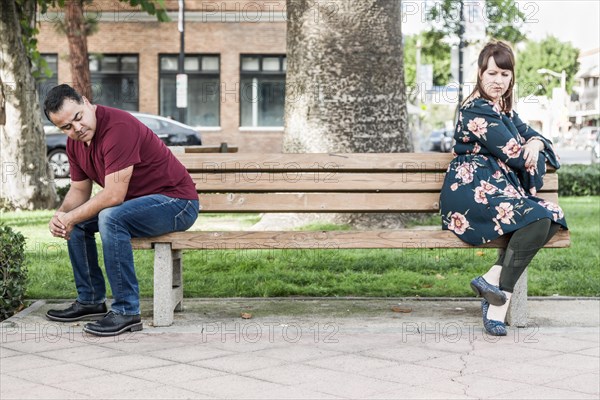 Unhappy mixed-race couple sitting facing away from each other on park bench