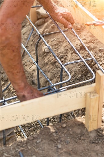Worker securing steel rebar framing with wire plier cutter tool at construction site