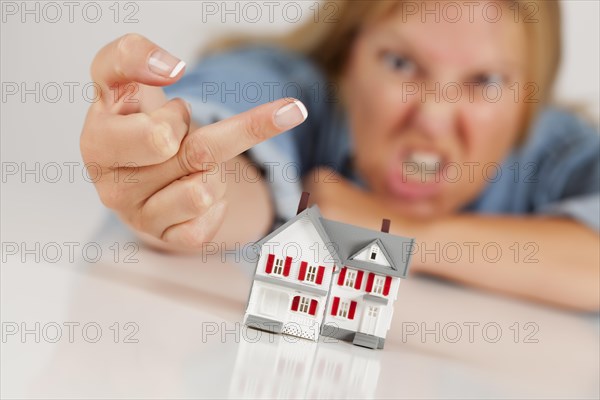 Angry woman flipping the bird behind model home on white surface