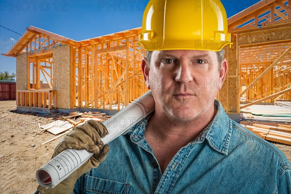 Serious contractor in hard hat holding floor plans at construction site