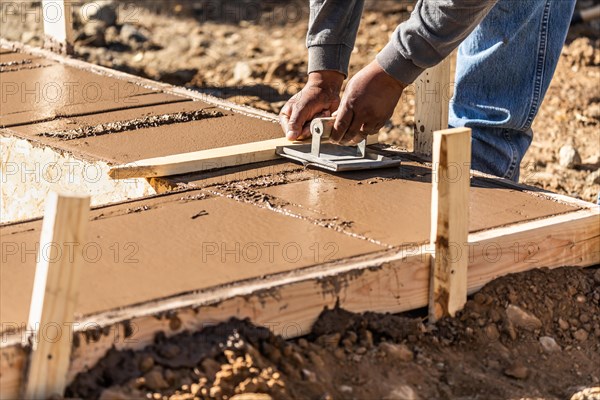 Construction worker using hand groover on wet cement forming coping around new pool