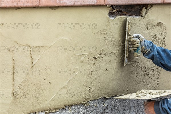 Tile worker applying cement with trowel at pool construction site