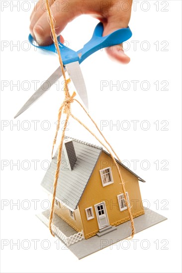 Hand with scissors cutting string holding house isolated on a white background