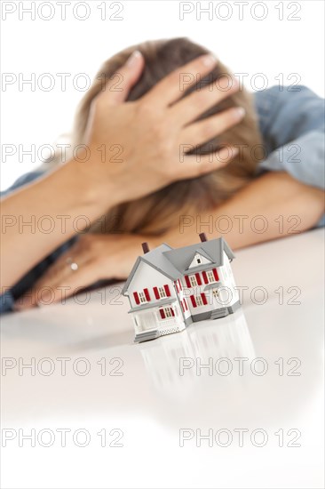 Woman with head in hand behind model home on a white surface