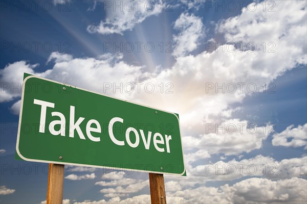 Take cover green road sign with dramatic clouds and sky