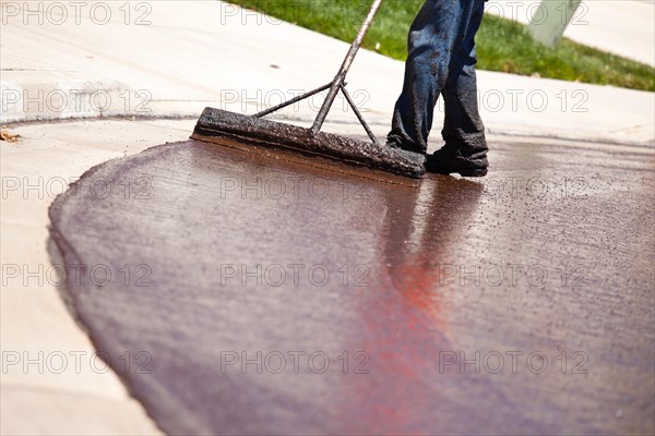 Road worker resurfacing street with hot tar