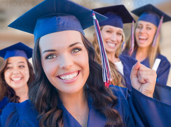 Happy graduating group of girls in cap and gown celebrating on campus