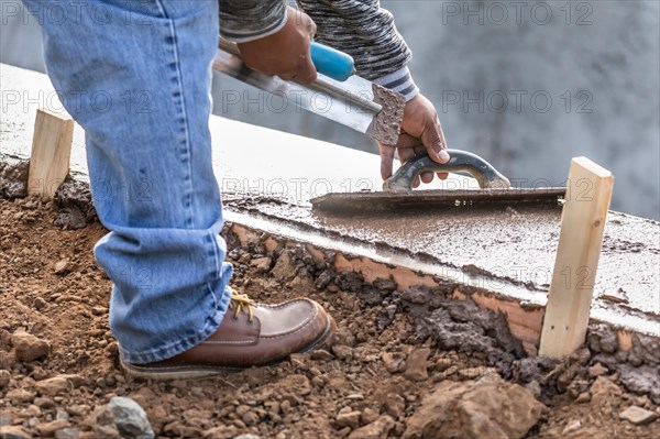 Construction worker using wood trowel on wet cement forming coping around new pool