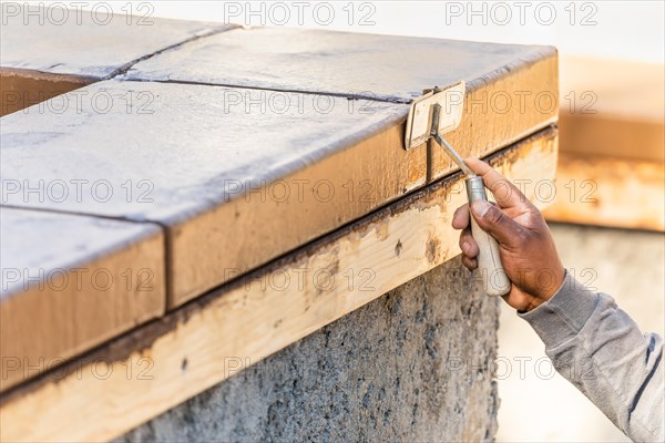 Construction worker using hand groover on wet cement forming coping around new pool