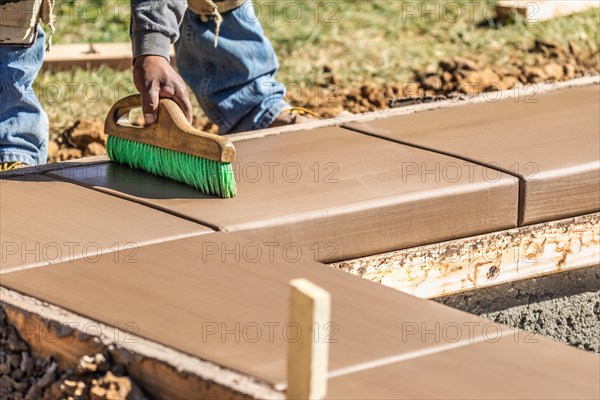 Construction worker using brush on wet cement forming coping around new pool