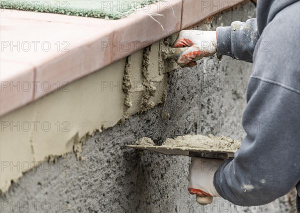 Tile worker applying cement with trowel at pool construction site