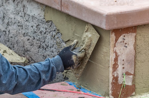 Tile worker applying cement with trowel at pool construction site