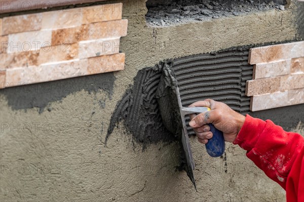 Worker installing wall tile cement with trowel and tile at construction site