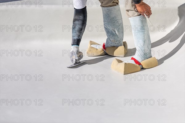 Worker wearing sponges on shoes smoothing wet pool plaster with trowel