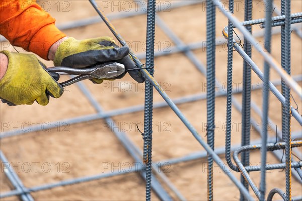 Worker securing steel rebar framing with wire plier cutter tool at construction site