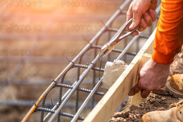 Worker securing steel rebar framing with wire plier cutter tool at construction site