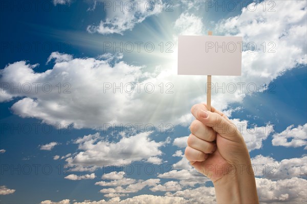 Man holding blank sign over dramatic clouds and blue sky with sun rays