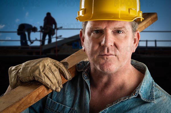 Serious contractor in hard hat carrying wood plank at construction site