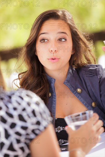 Expressive young adult woman having drinks and talking with her friend outdoors