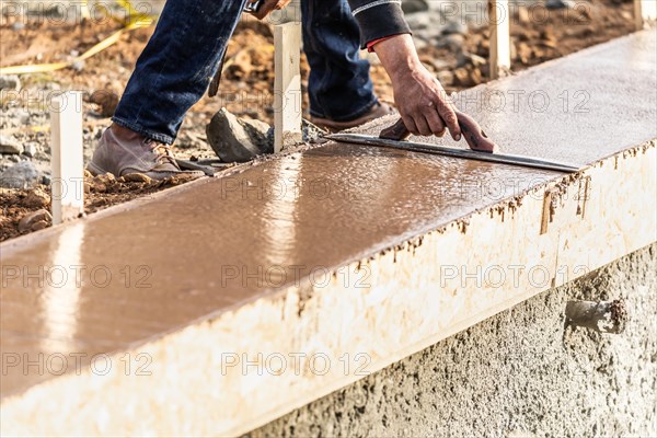 Construction worker using wood trowel on wet cement forming coping around new pool