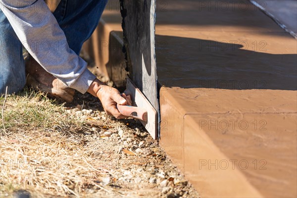 Construction worker applying pressure to texture template on wet cement