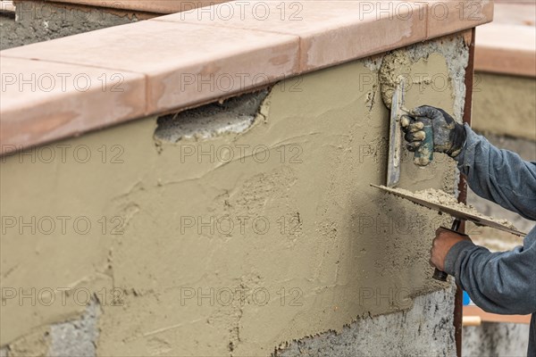 Tile worker applying cement with trowel at pool construction site